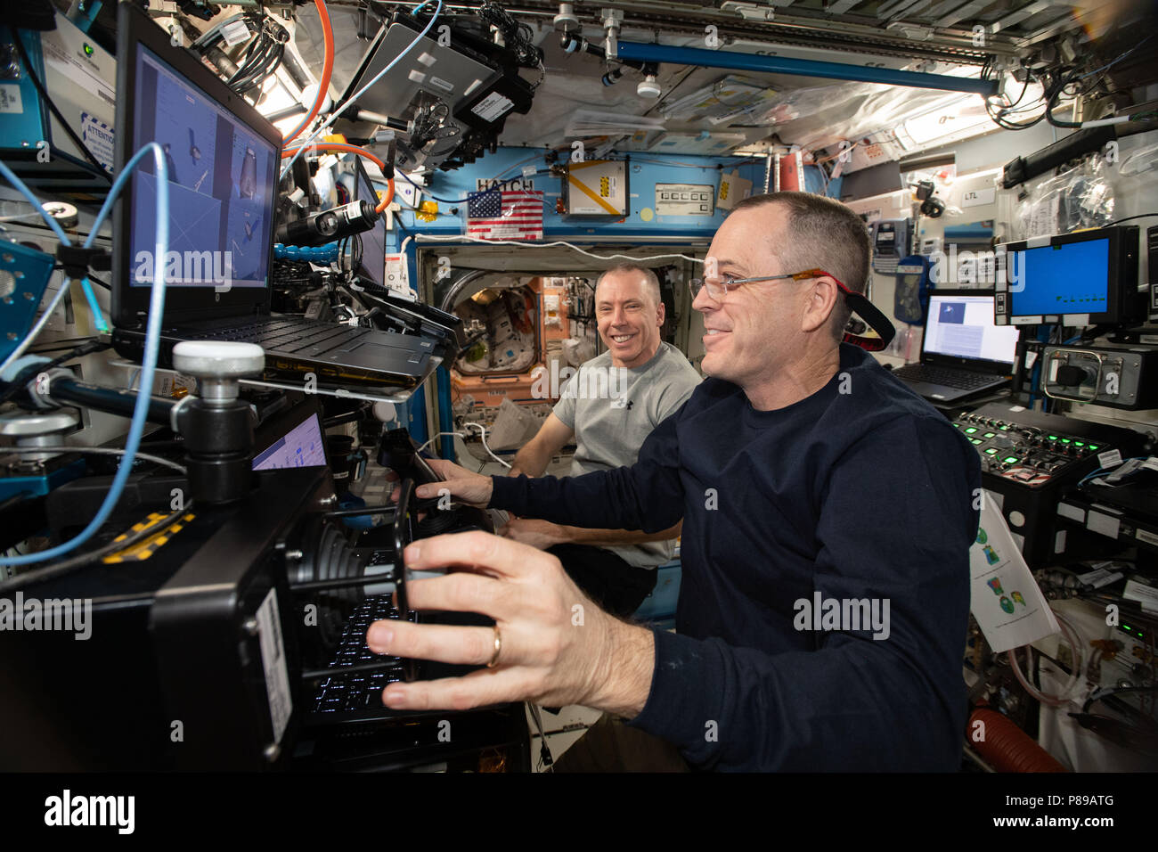 NASA astronauts Ricky Arnold, foreground, and Drew Feustel practice on a simulator before their upcoming robotic maneuvers to capture the SpaceX Dragon commercial cargo spaceship as it arrives at the International Space Station June 26, 2018 in Earth Orbit. Stock Photo