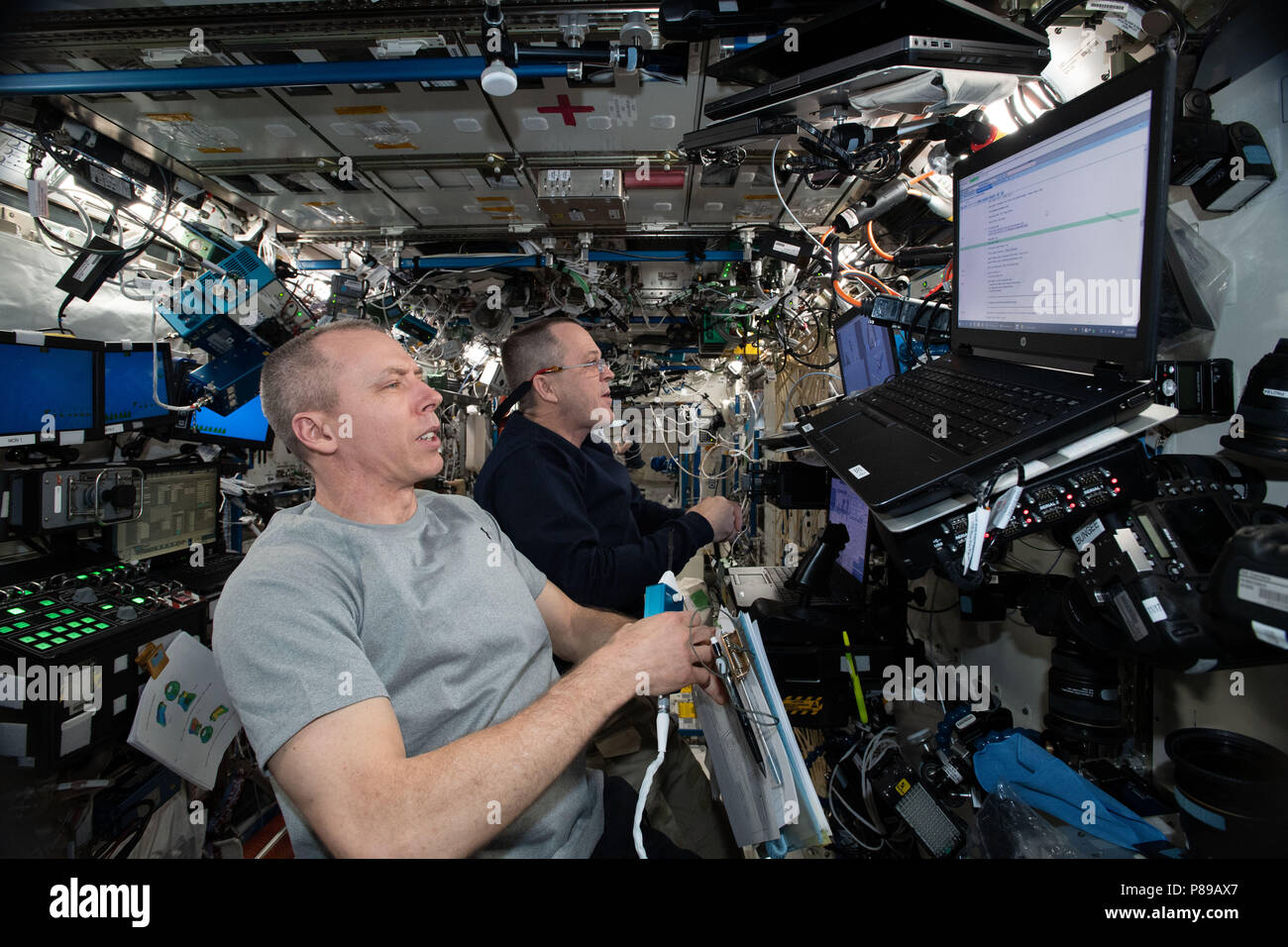 NASA astronauts Drew Feustel, foreground, and Ricky Arnold practice on a simulator before their upcoming robotic maneuvers to capture the SpaceX Dragon commercial cargo spaceship as it arrives at the International Space Station June 26, 2018 in Earth Orbit. Stock Photo