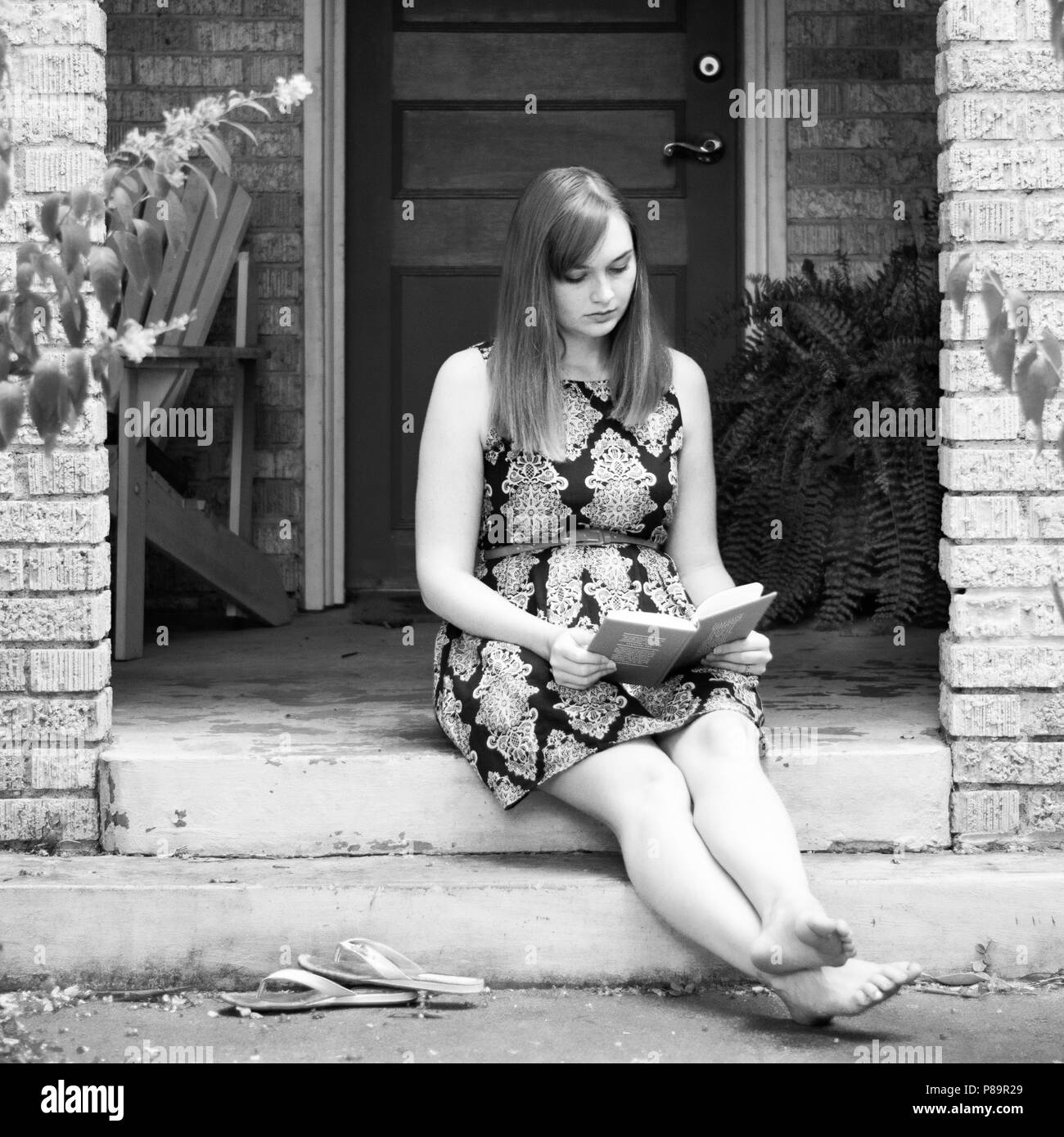 Young woman sitting on stoop reading book in black and white Stock Photo