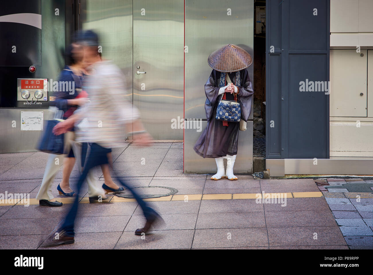 A Shintoist monk asking for alms in the street in Fukuoka, Japan, surrounded by motion blurred pedestrians. Stock Photo
