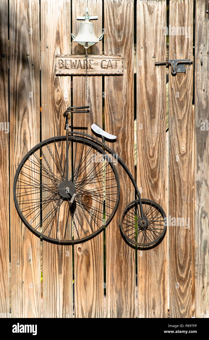 High Wheeled old fashioned bicycle, also called a Penny Farthing, decorates a wooden gate door in Key West, Florida. Beware-of-Cat sign hangs above. Stock Photo
