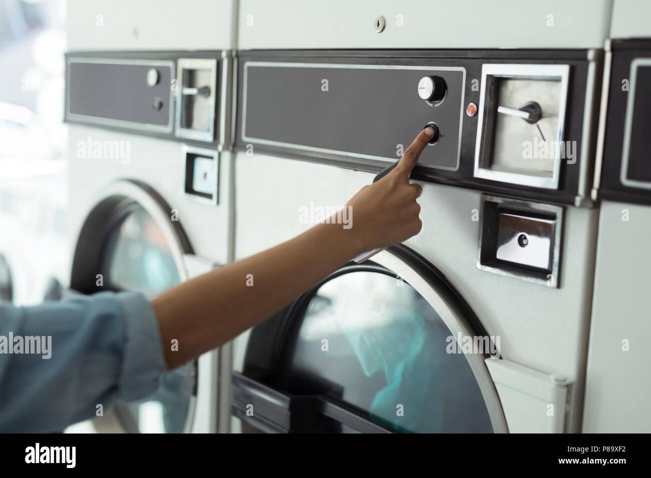 Woman operating washing machine at laundromat Stock Photo Alamy