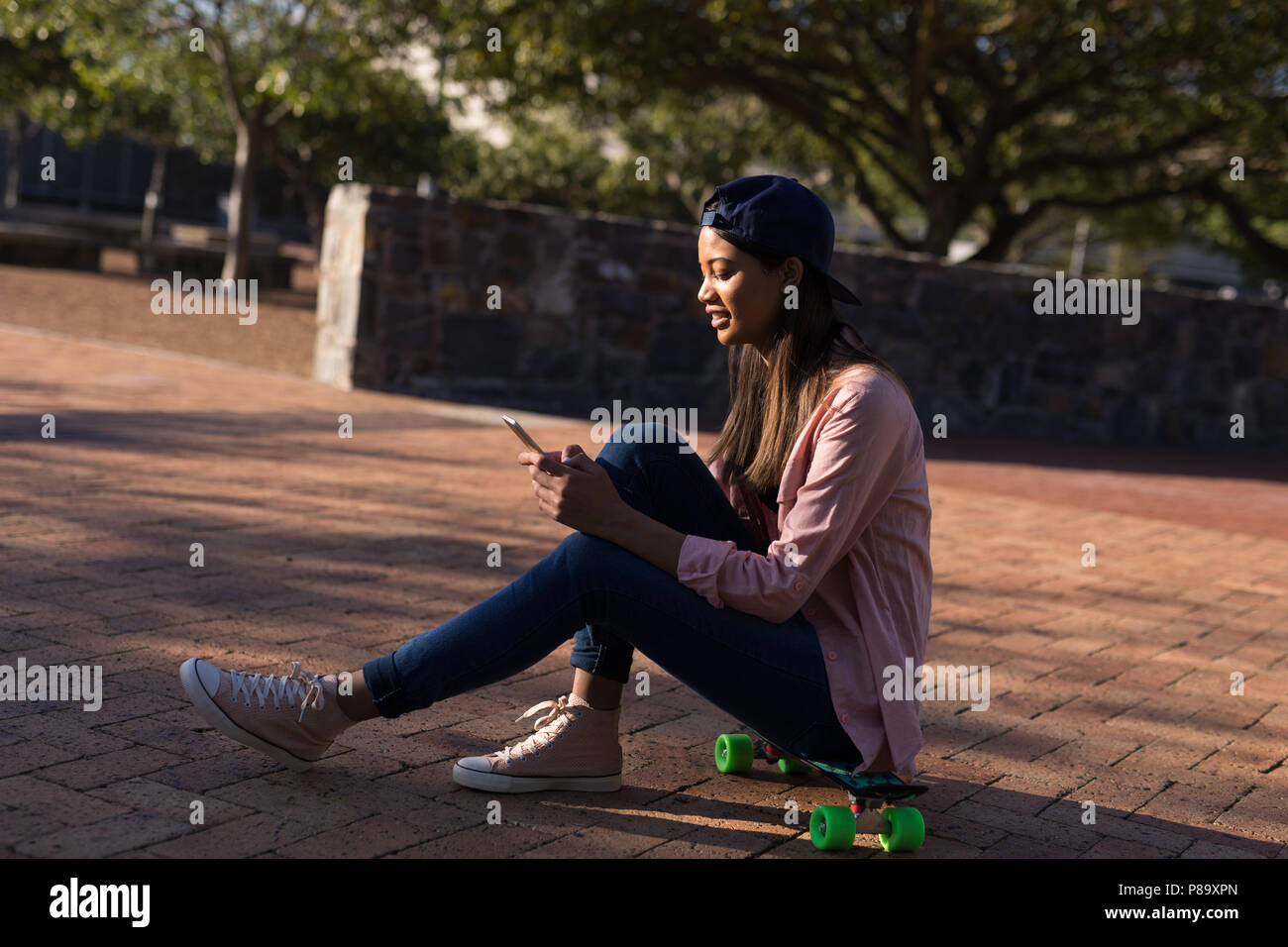 Woman sitting on the skateboard using mobile phone Stock Photo