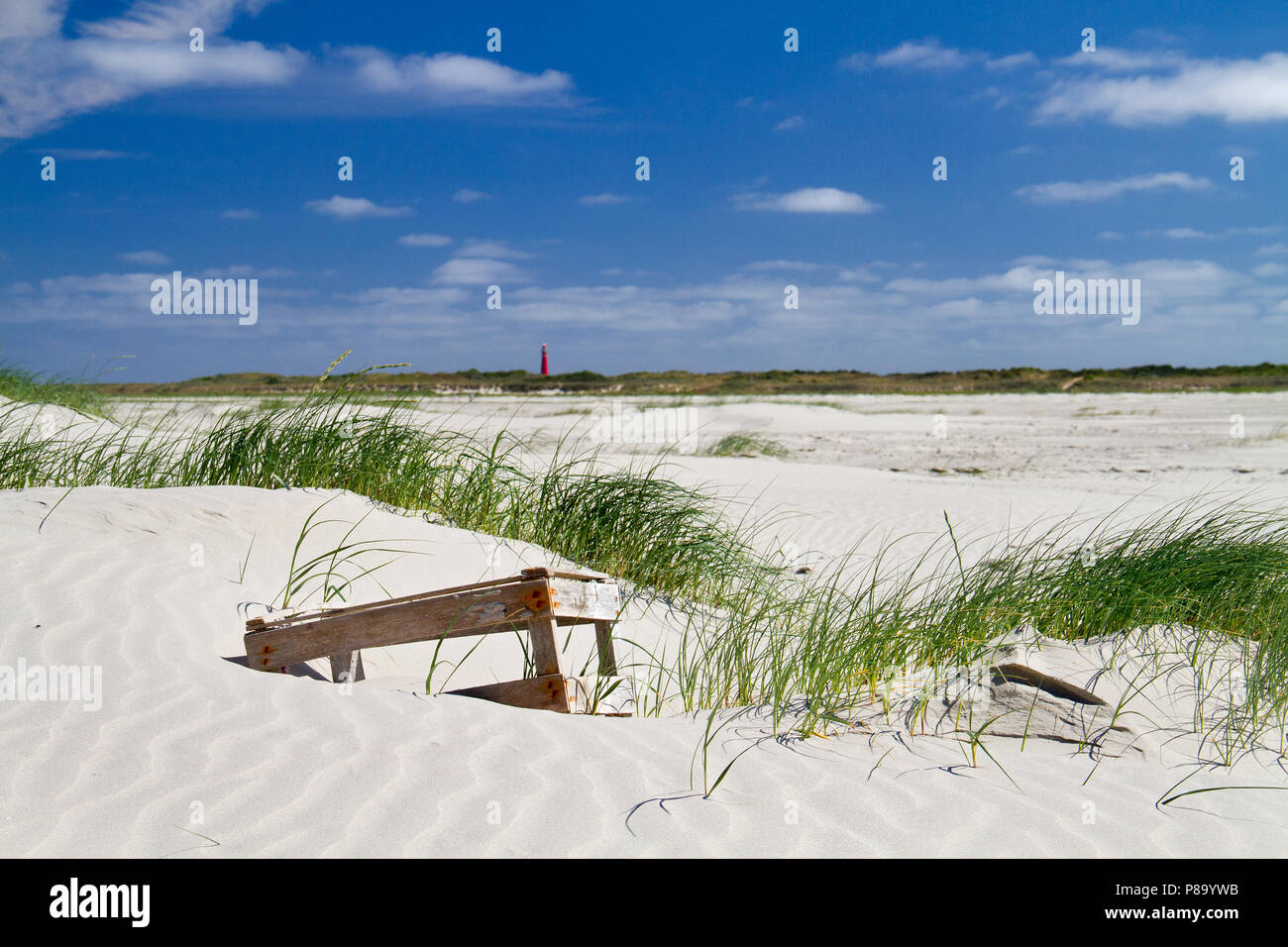 A wooden crate, washed ashore, lying in the sand of a new formed dune, in the distance a red lighthouse Stock Photo