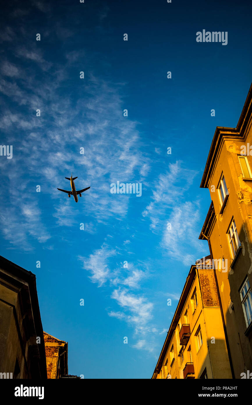 Passenger jet plane is flying over street in downtown Sofia, Bulgaria. Blue sky with some white clouds, old brown brick residential buildings, image taken at sunset Stock Photo