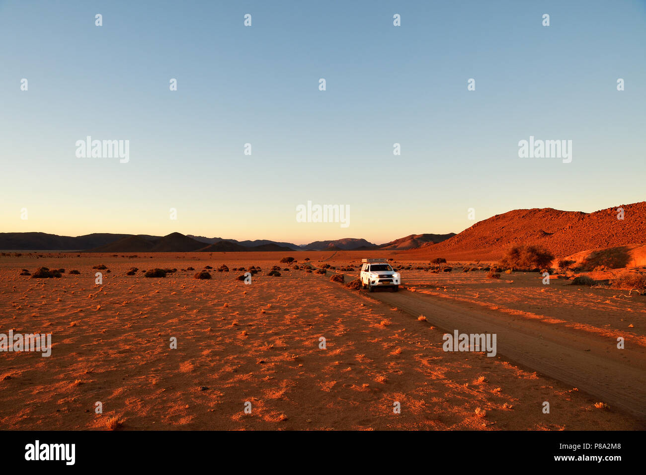 All-terrain vehicle drives on sandtrack in the evening light, behind Tiras Mountains, Namibia Stock Photo