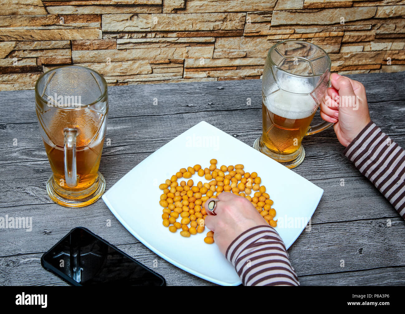A woman sitting in a bar, drinking light beer and eating salted nuts. Stock Photo