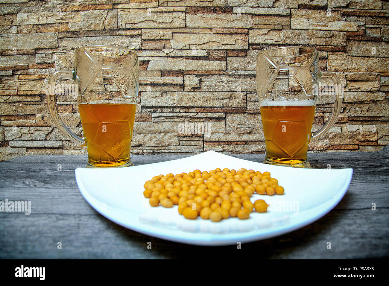 On the wooden table in the beer bar there are two large glasses of cold light beer and a plate with salted nuts. Stock Photo