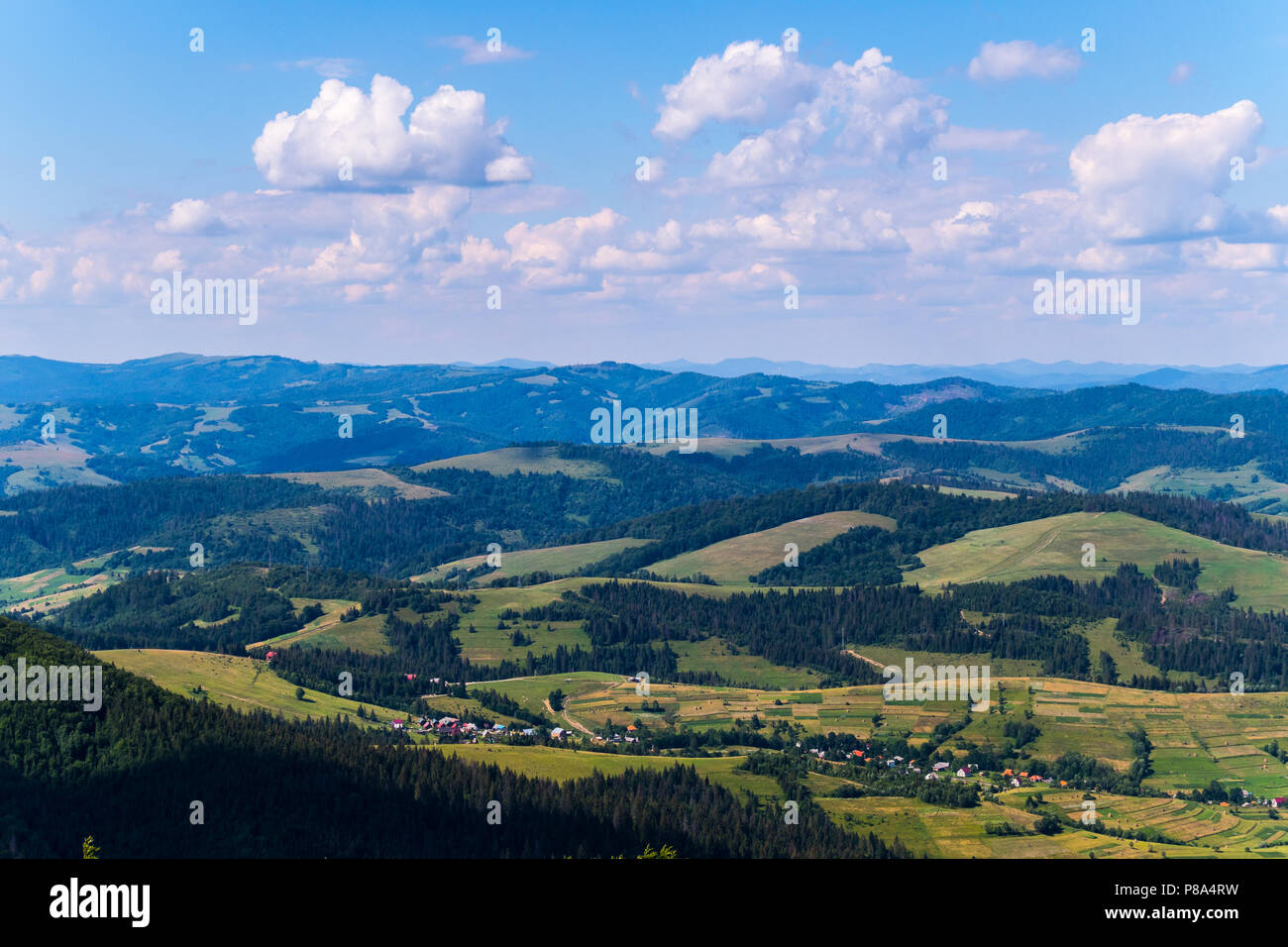 village in a mountain valley, green trees and blue sky with clouds ...