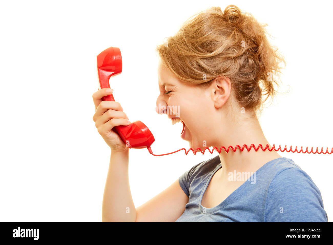 Young angry woman loudly roars in a red telephone receiver Stock Photo