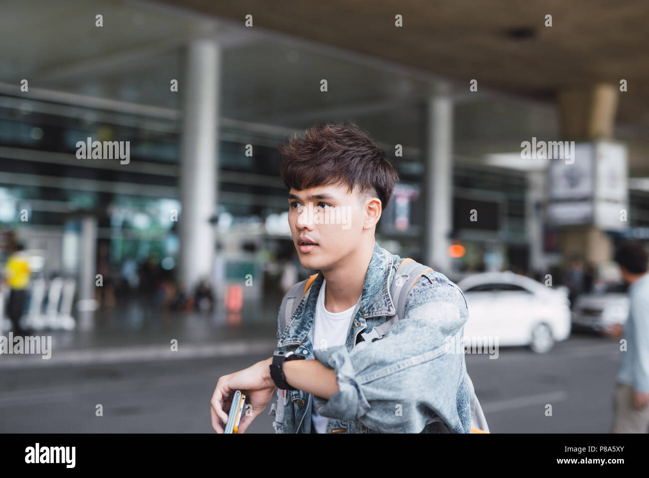Young asian man looking at his watch in front at the airport terminal Stock Photo