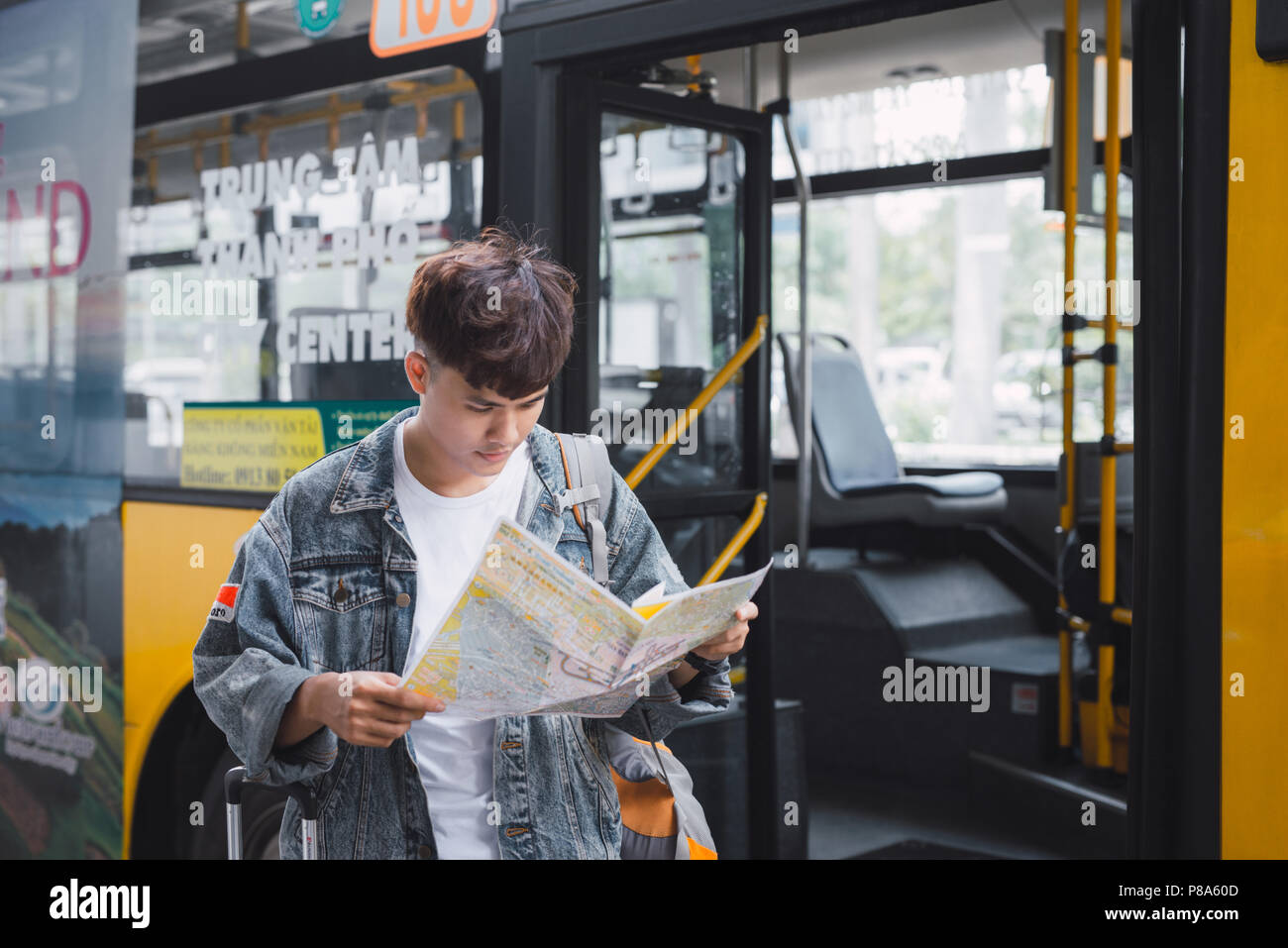 Young man handsome with luggage bag on city street with busy traffic transport looking map, waiting for public bus Stock Photo