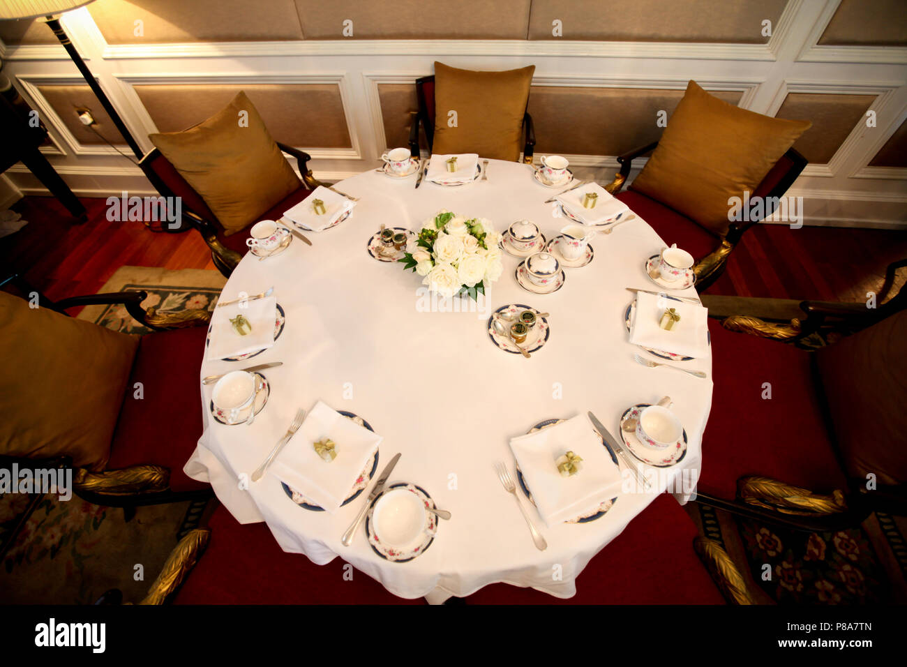 High-angle shot of a big round table, laid with an English Afternoon Tea table setting, jam and a flower bouquet on a white table cloth in a... Stock Photo