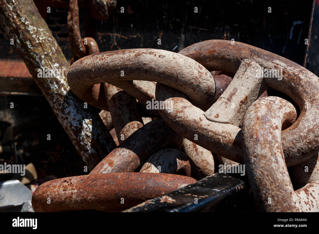 Close-up of a huge, heavy, rusted chain lying in a sunlit pile ...
