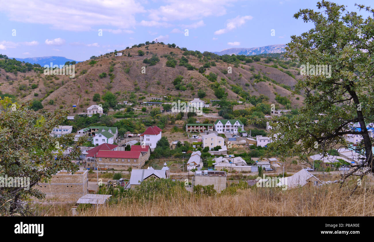 small unpretentious town at the foot of a rocky hill on the background of the distant mountains . For your design Stock Photo