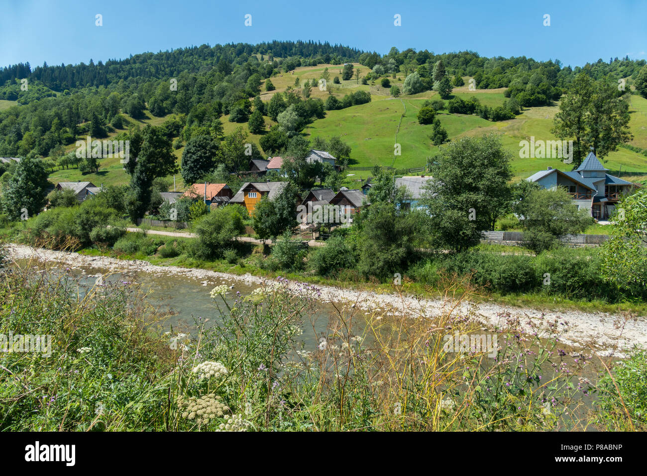 The village street with neat houses is located at the foot of the hill with green slopes and the current below the river. . For your design Stock Photo