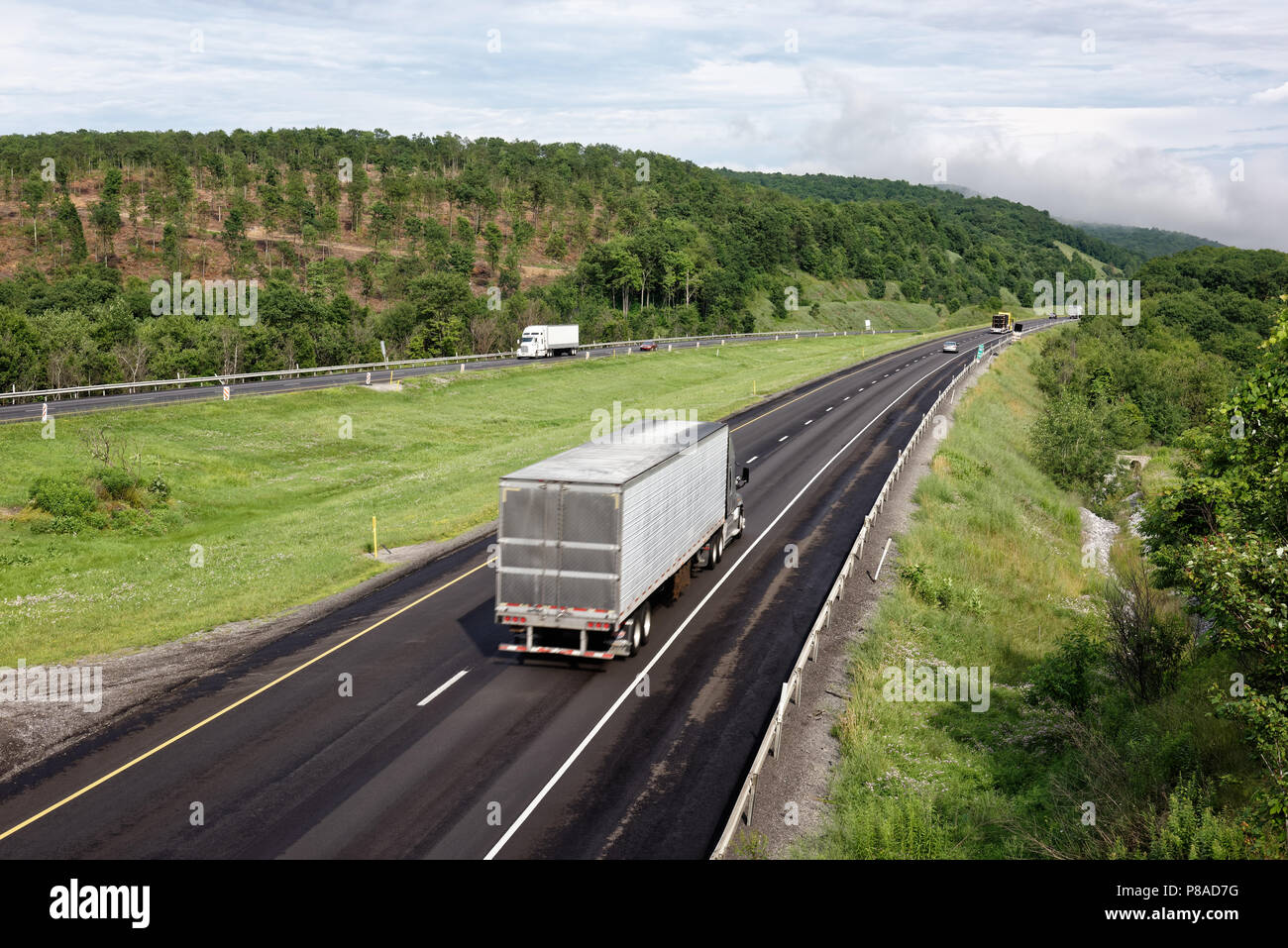 Trucks moving down interstate highway through scenic eastern mountains, tractor trailers in trucking industry hauling freight, some motion blur. Stock Photo