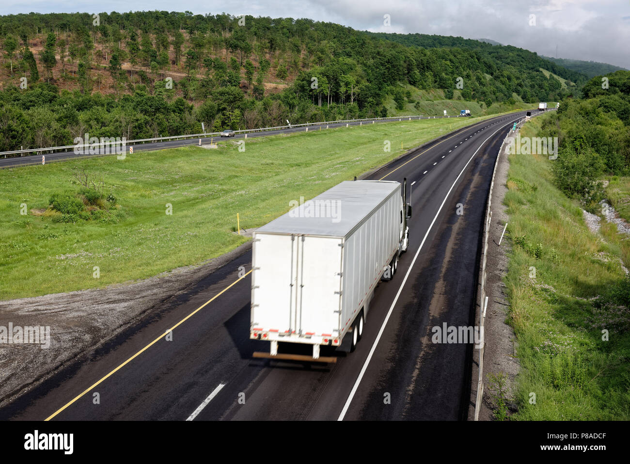 Trucks moving down interstate highway through scenic eastern mountains, tractor trailers in trucking industry hauling freight, some motion blur. Stock Photo