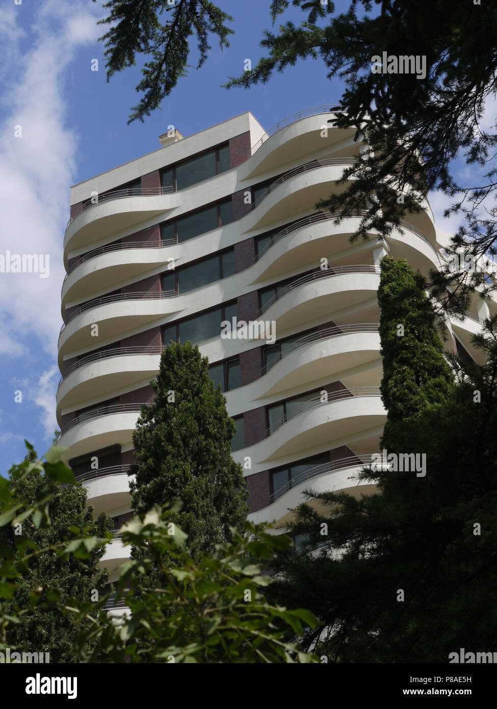 A beautiful high-rise hotel with semi-circular balconies with firs growing below the trees and other trees. . For your design Stock Photo