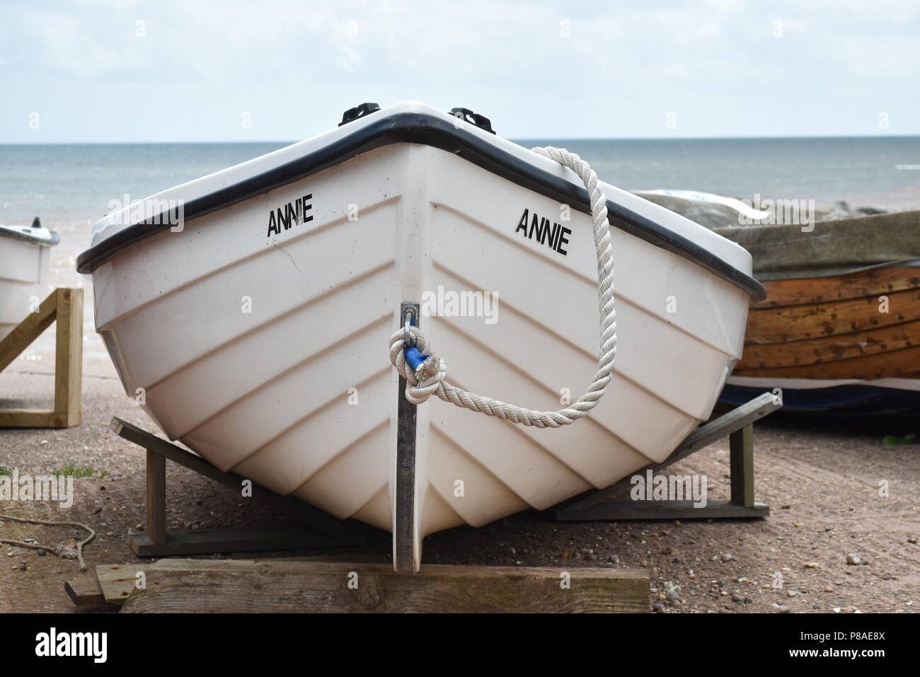 The bow of a small white  boat named Annie resting on supports near the sea shore with the sea in the background at Sidmouth, Devon , England Stock Photo