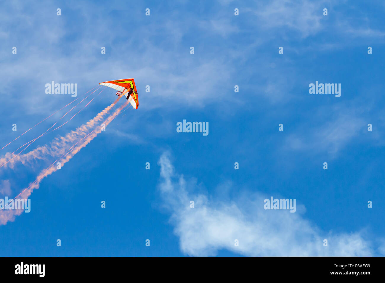 Hang glider with smoke trails and streamers against a blue sky with some cloud cover. Lots of copyspace available Stock Photo