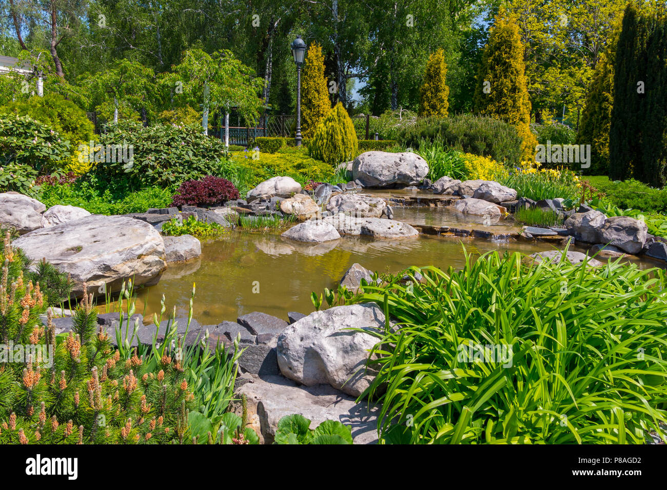 decorative pond surrounded by boulders, flowers, green bushes ...