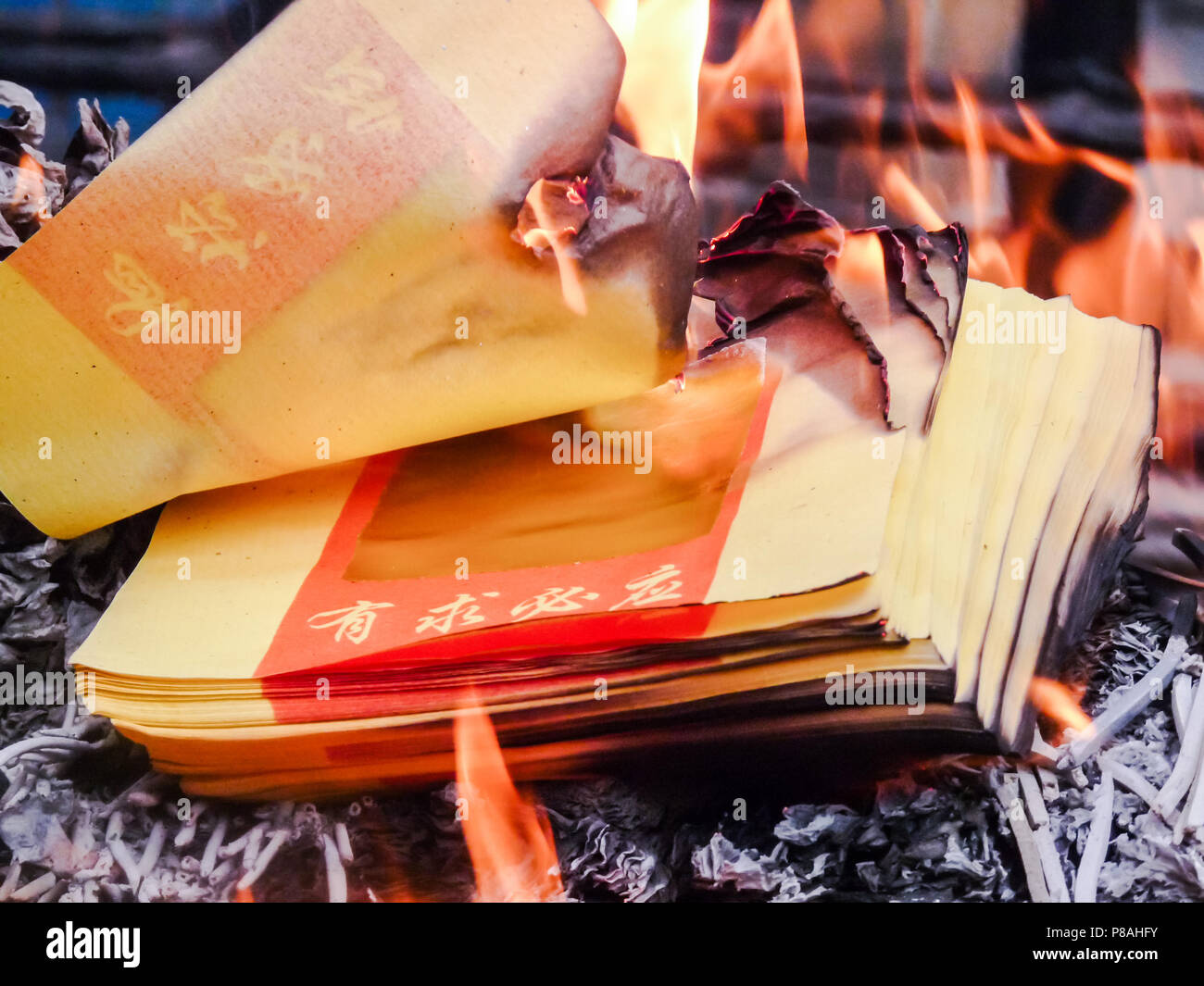 Burning Chinese joss paper or ghost money at a temple during Chinese lunar new year. The paper says ' all request will be granted'. Stock Photo