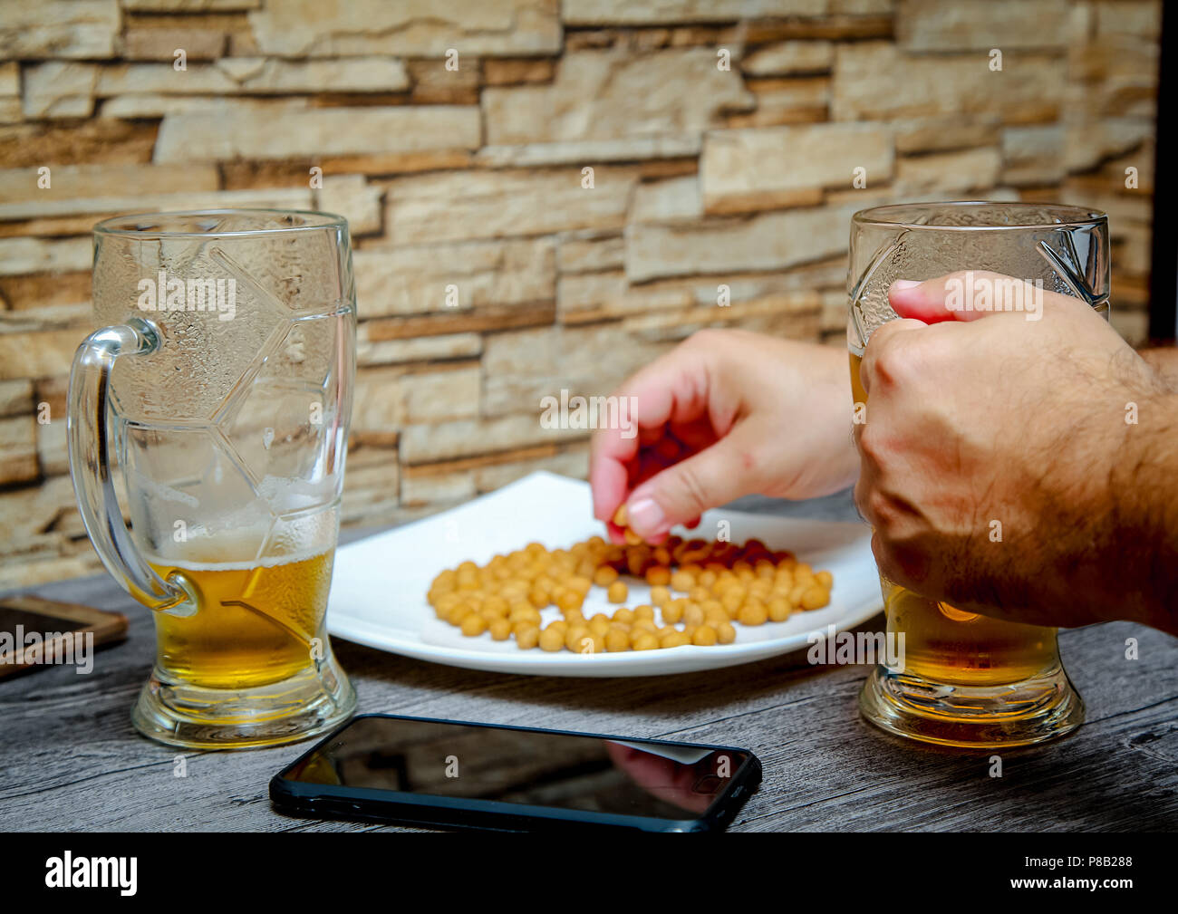 Close-up of men's hands holding a glass of beer and taking nuts from a plate. Stock Photo
