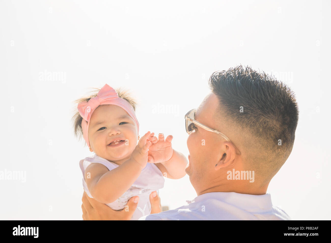 Young Man Father Holds his Cute Laughing Baby Toddler Daughter in Hands Throws up in the Air. Soft Summer Sunlight. Genuine Authentic Emotions Candid  Stock Photo