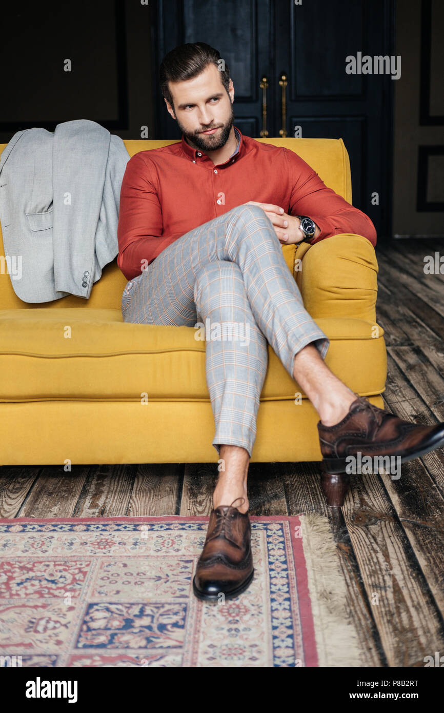 elegant man in suit and brogue shoes sitting on yellow sofa Stock Photo