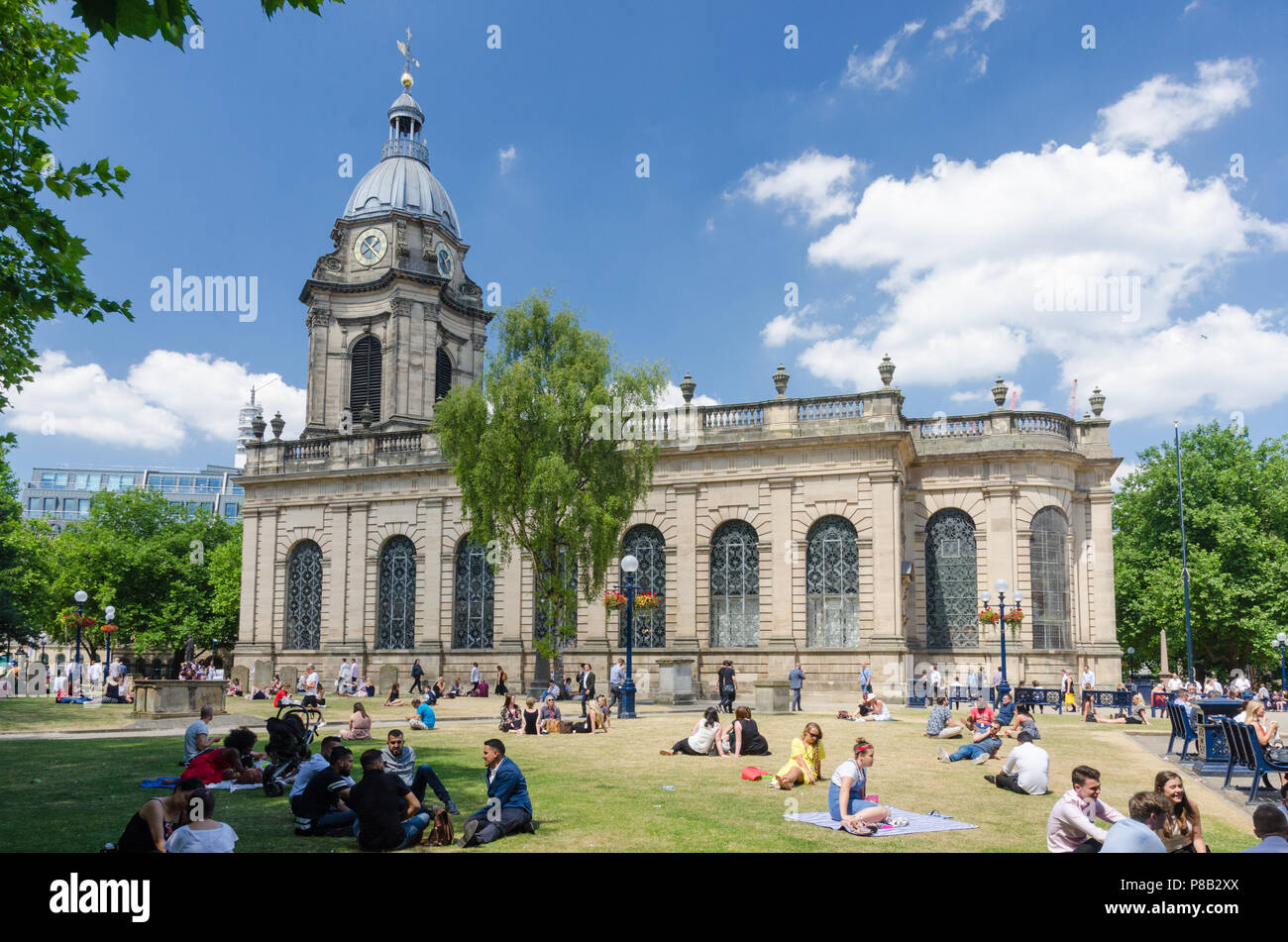 Office workers sit outside at lunchtime in the warm summer sunshine in the grounds surrounding St Philip's Cathedral in Birmingham Stock Photo