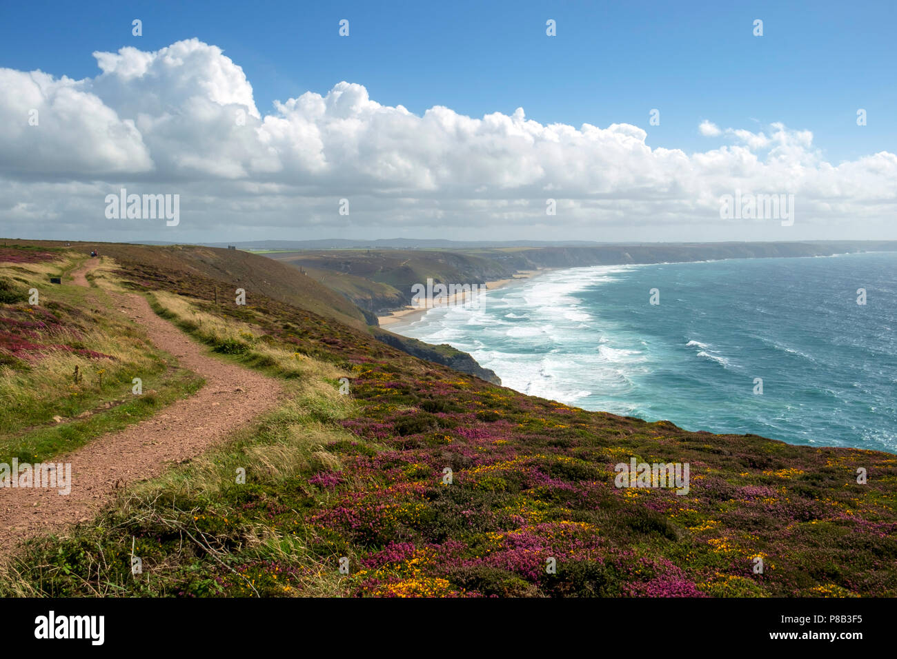 Couples in the distance walk the footpaths on the St Agnes Heritage Coast towards Chapel Porth Beach on a sunny summer afternoon in Cornwall, UK Stock Photo