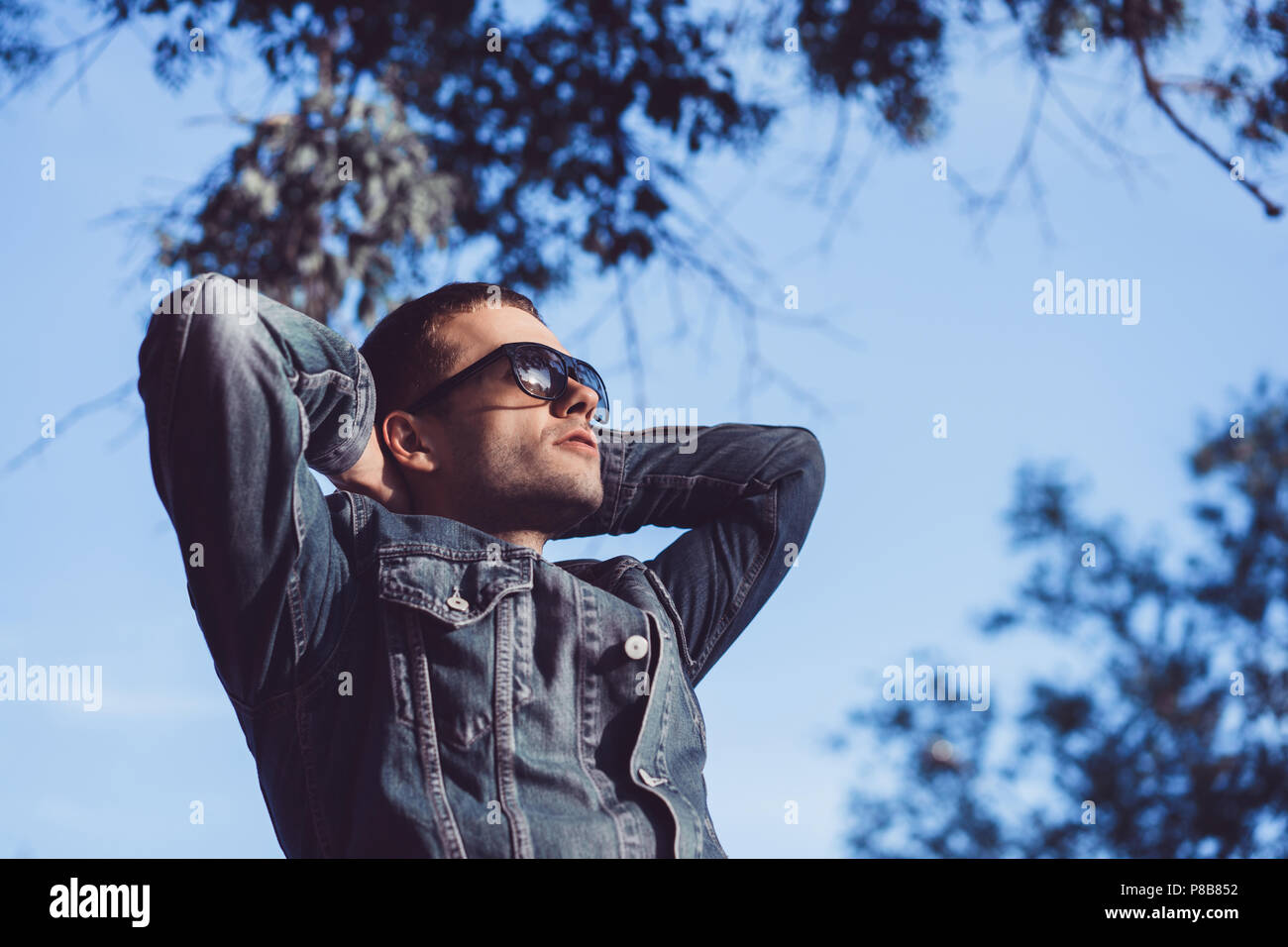 Man in sunglasses standing with hands by head on sky background Stock ...