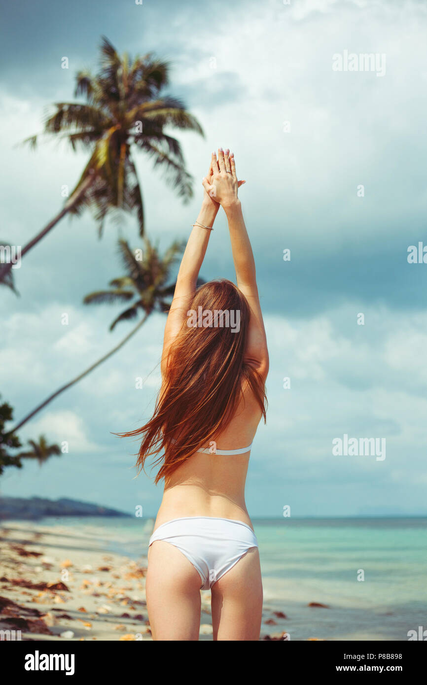 back view of woman in bikini standing on beach near ocean Stock Photo