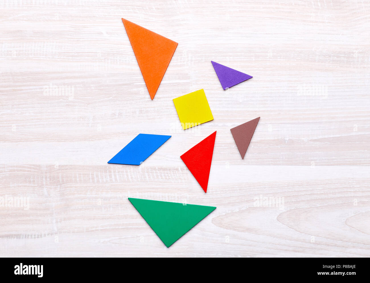 Colored geometric pieces of puzzle like triangles, square and parallelogram, are scattered on a light wooden background Stock Photo