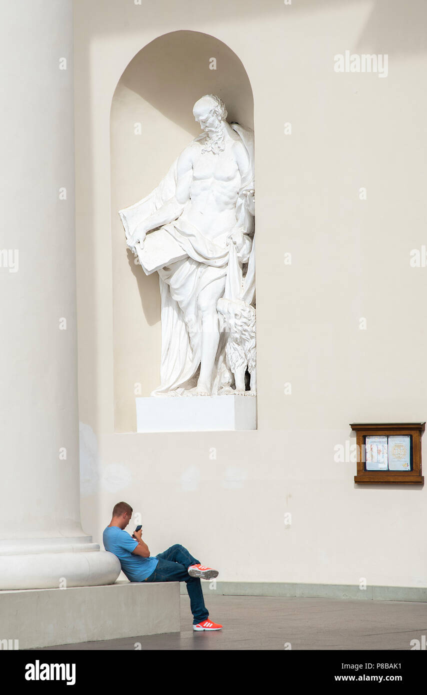 Man uses his mobile phone next to a statue outside Vilnius Cathedral, Lithuania Stock Photo