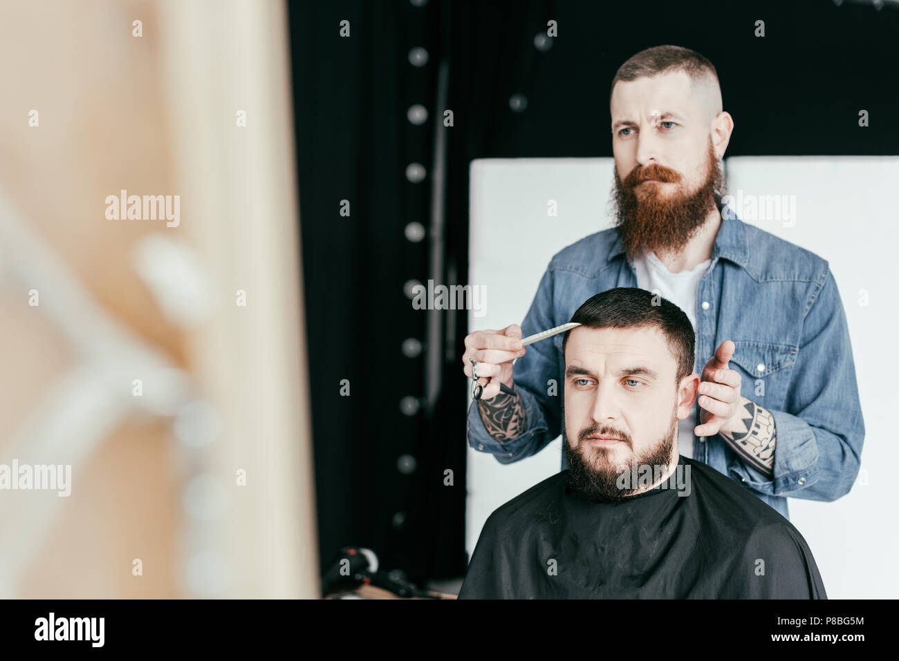 barber looking at customer haircut in mirror at barbershop Stock Photo