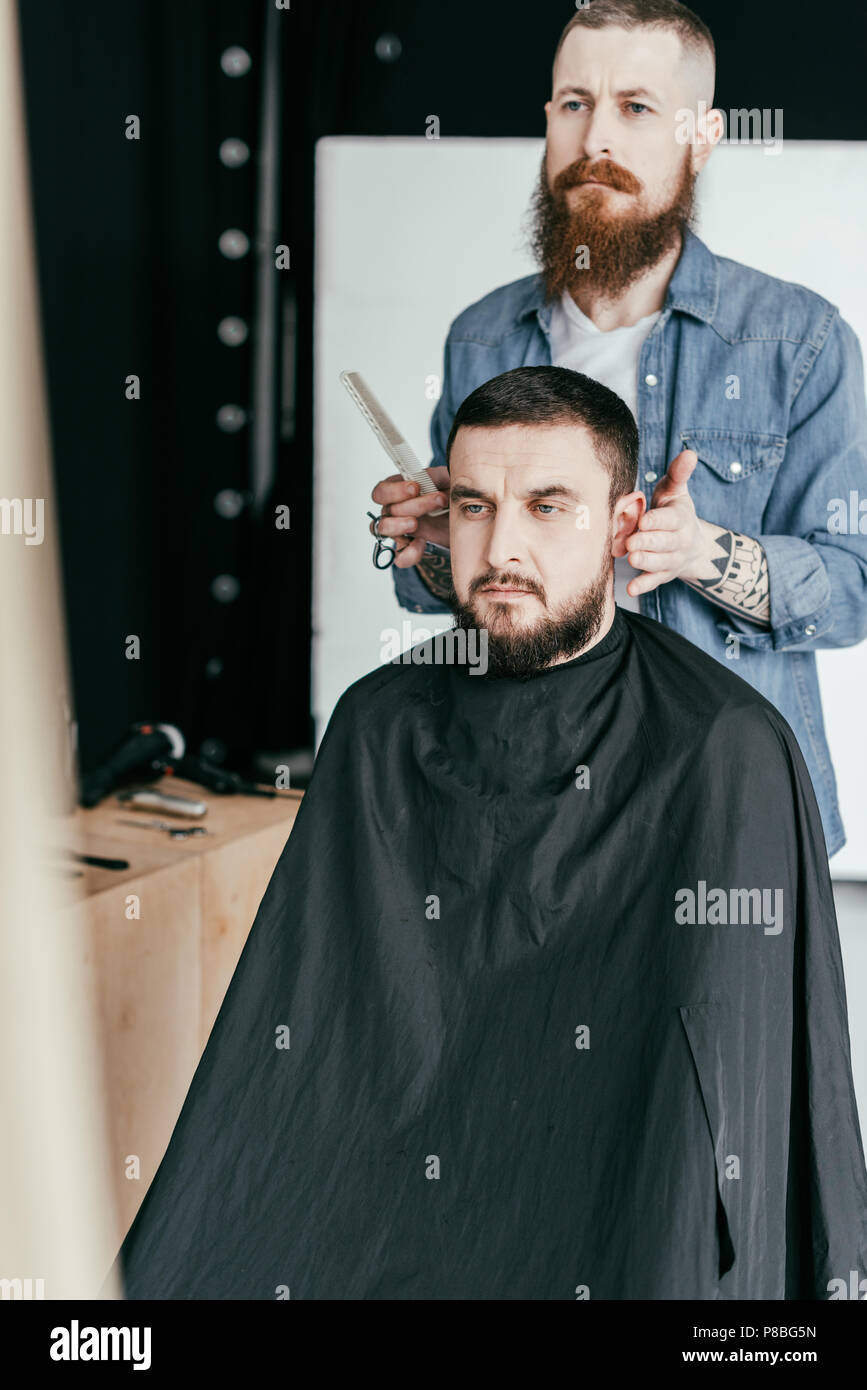 barber looking at client haircut in mirror at barbershop Stock Photo