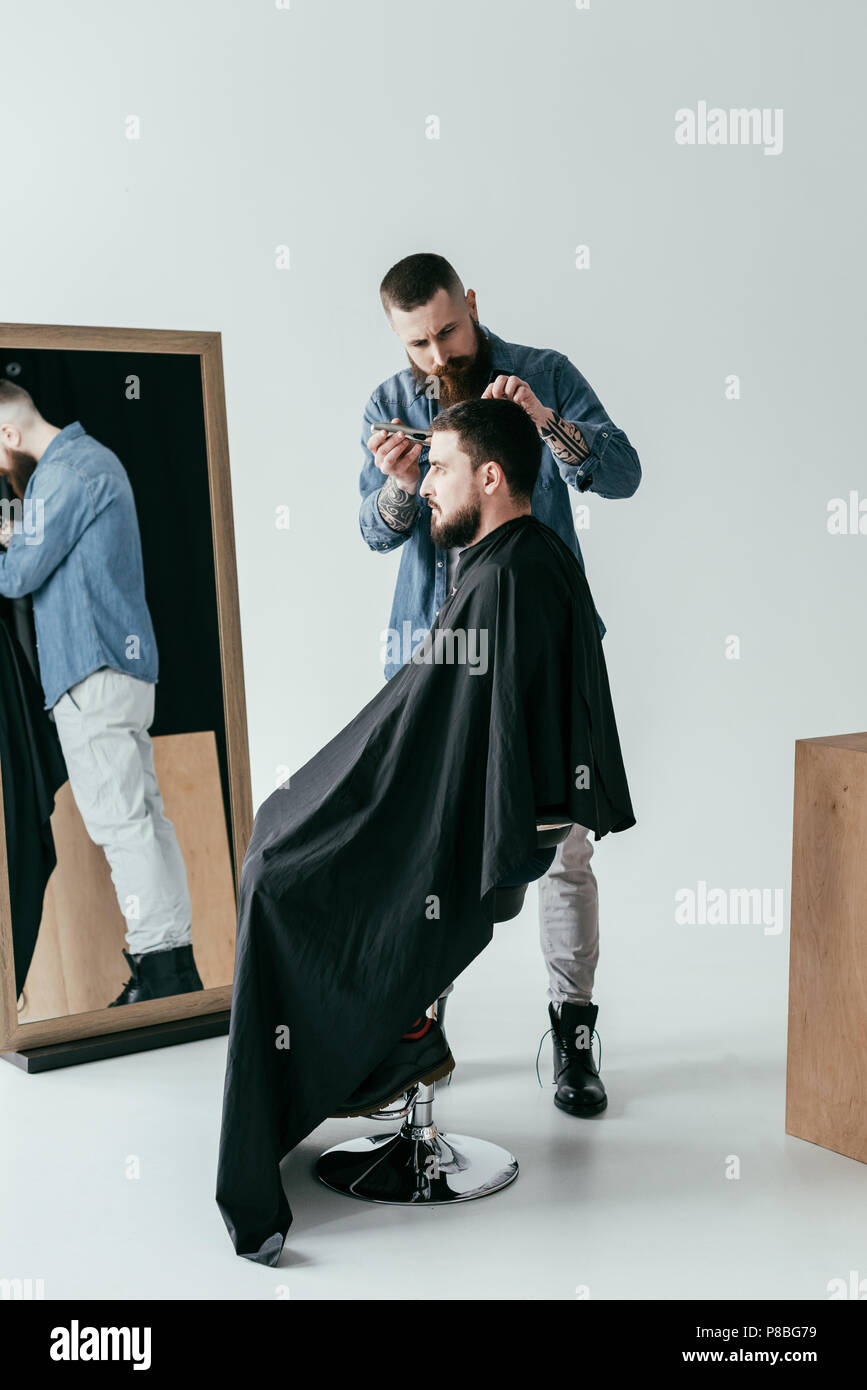 barber shaving customer hair in front of mirror at barbershop Stock Photo