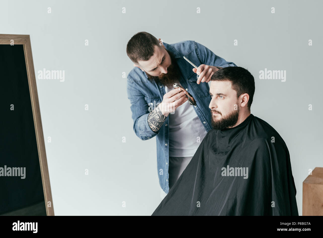 barber trimming handsome customer beard at barbershop isolated on white Stock Photo