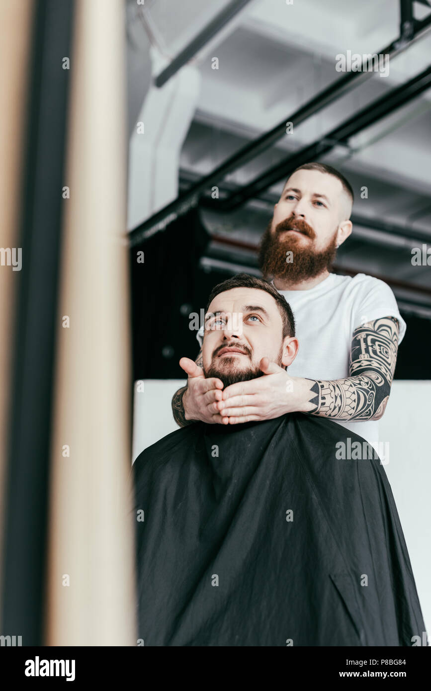 barber styling customer beard and looking at mirror at barbershop Stock Photo