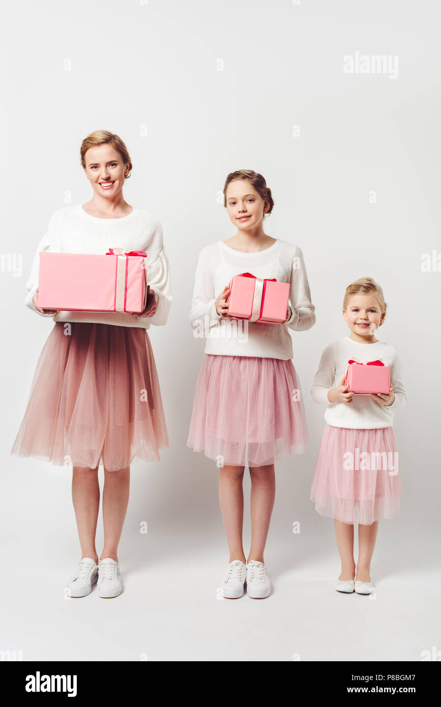 smiling mother and little daughters in similar pink tutu tulle skirts with wrapped gifts isolated on grey Stock Photo