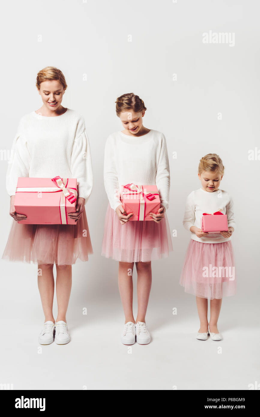 smiling mother and little daughters in similar pink tutu tulle skirts with wrapped gifts isolated on grey Stock Photo