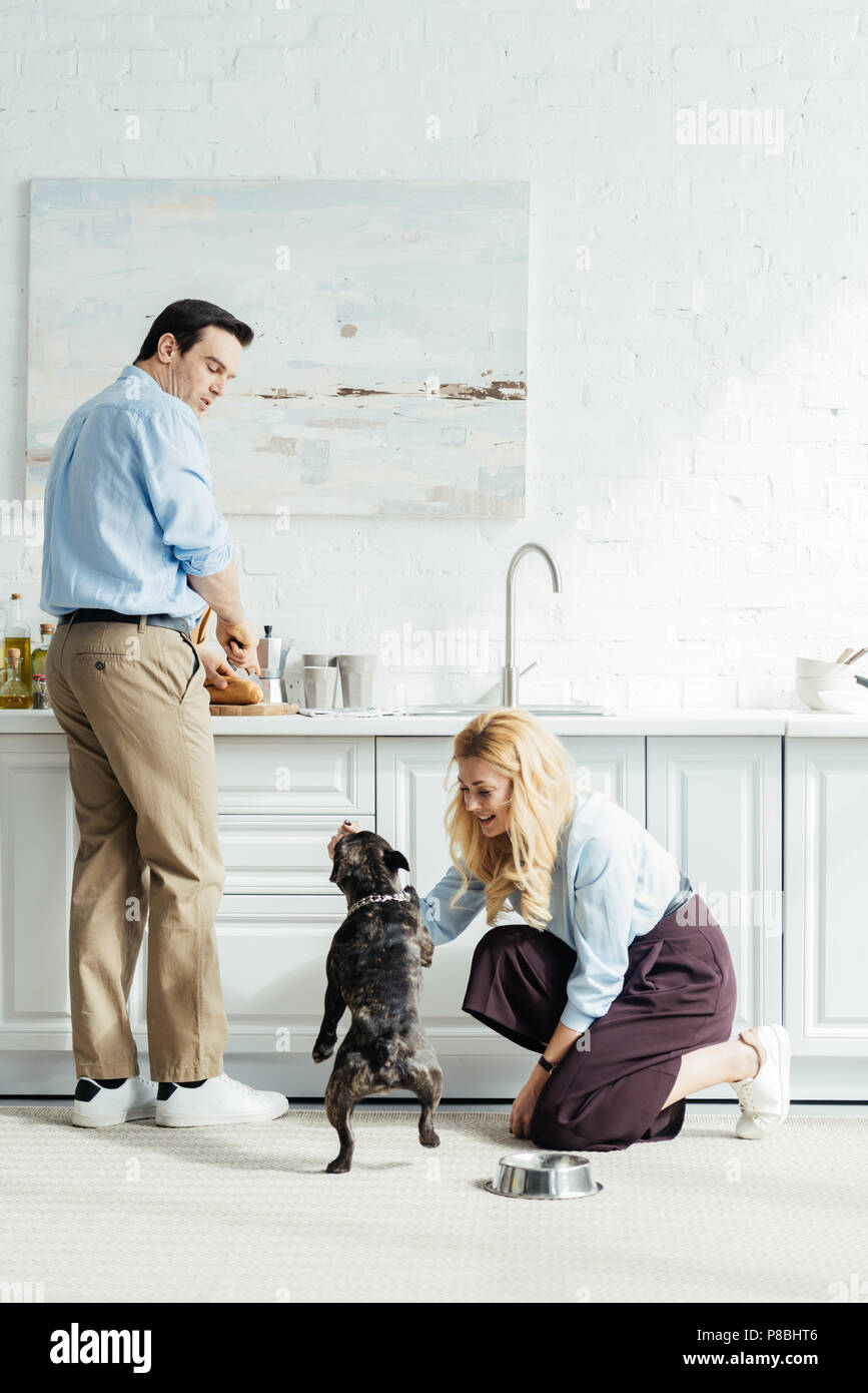 Man preparing food and woman playing with french bulldog on kitchen floor Stock Photo