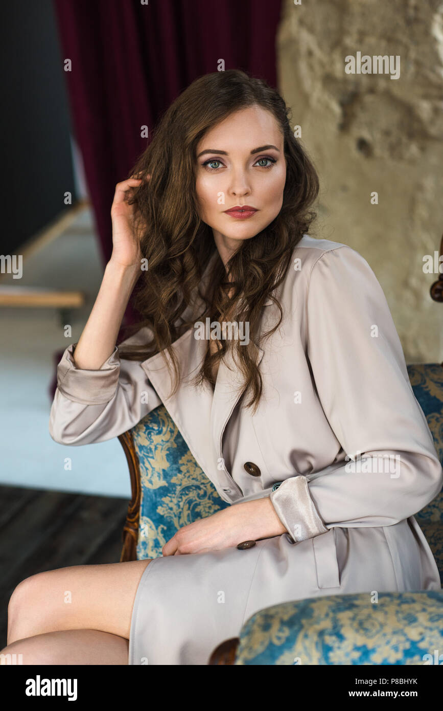 elegant woman in fashionable trench coat sitting in armchair Stock ...