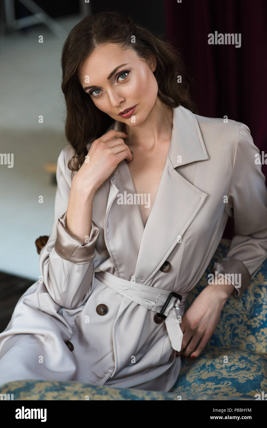 attractive woman in trench coat sitting in armchair Stock Photo - Alamy