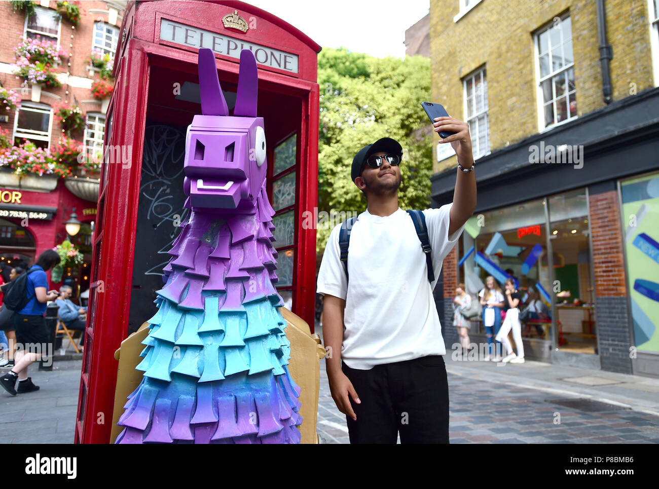 A man takes a selfie with a Fortnite Loot Llama in a red telephone ...