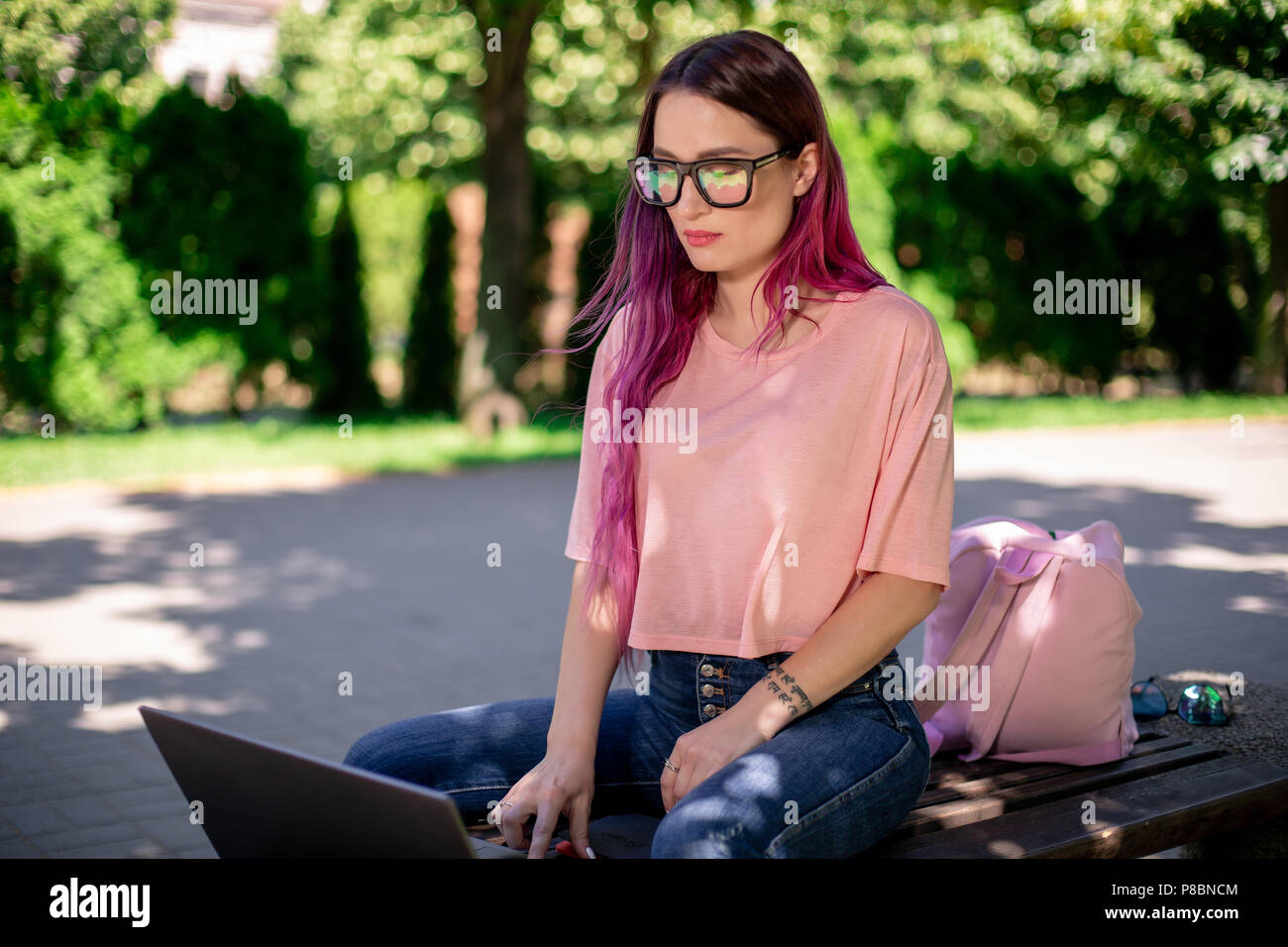 Young girl is studying in the spring park, sitting on the wooden bench and browsing on her laptop Stock Photo