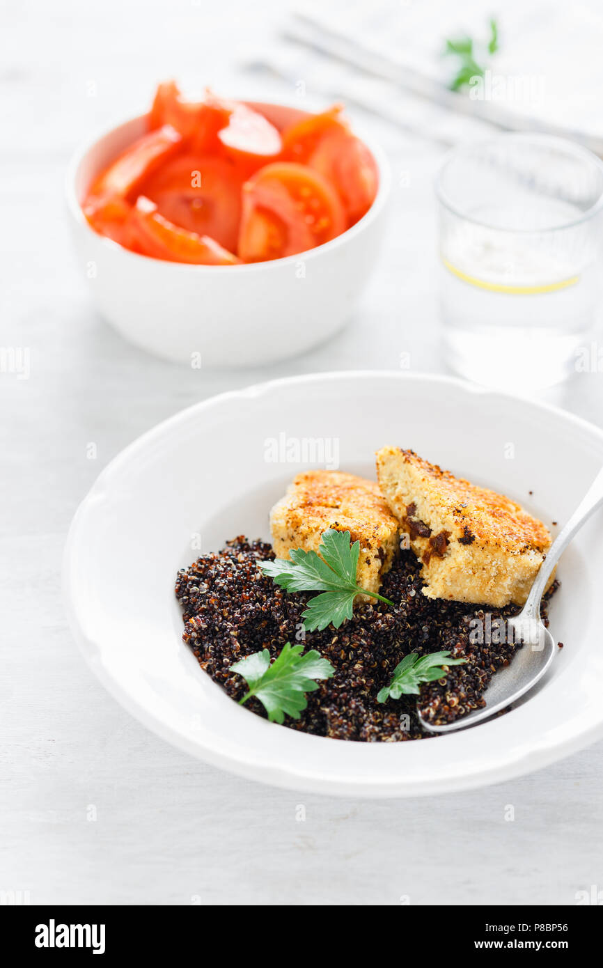 Vegetarian dinner table. Plate with black quinoa and oatmeal cutlets with prunes on white wooden table with tomato salad and water with lemon, top vie Stock Photo