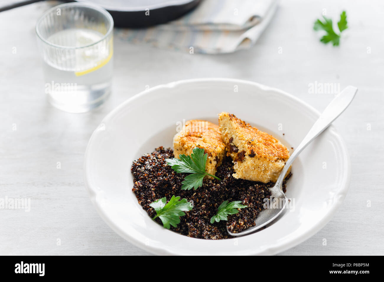Vegetarian dinner table. Plate with black quinoa and oatmeal cutlets with prunes on white wooden table with lemon water close up Stock Photo